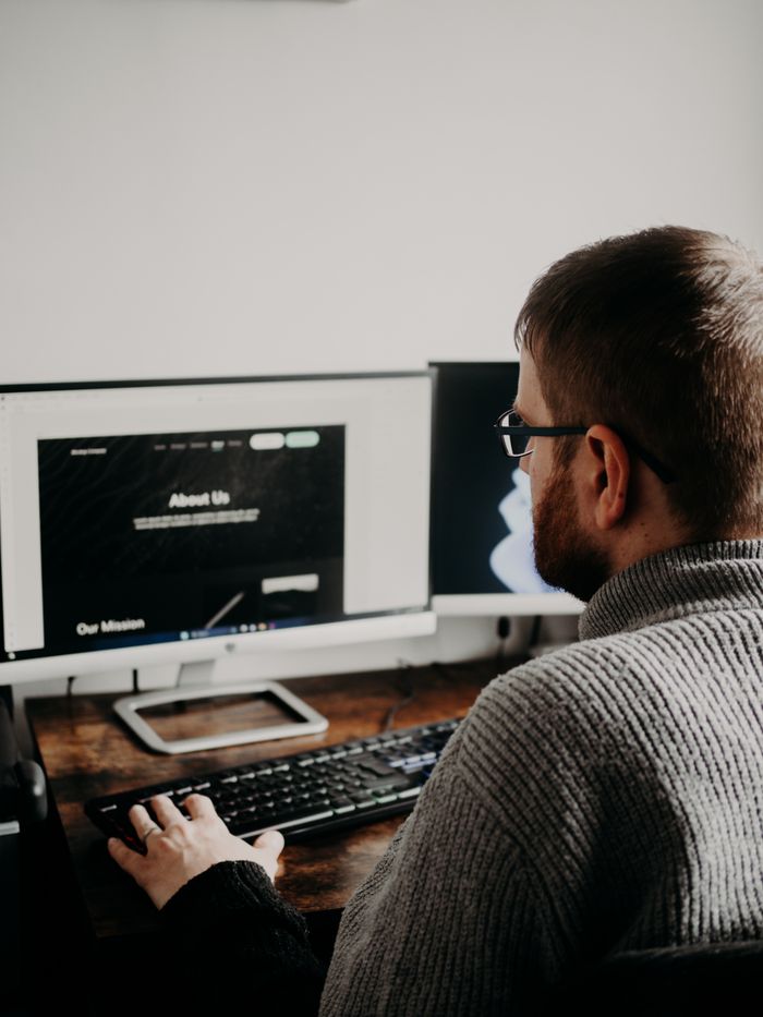 creative-01 A man is working on web design from a home office setup with two monitors.